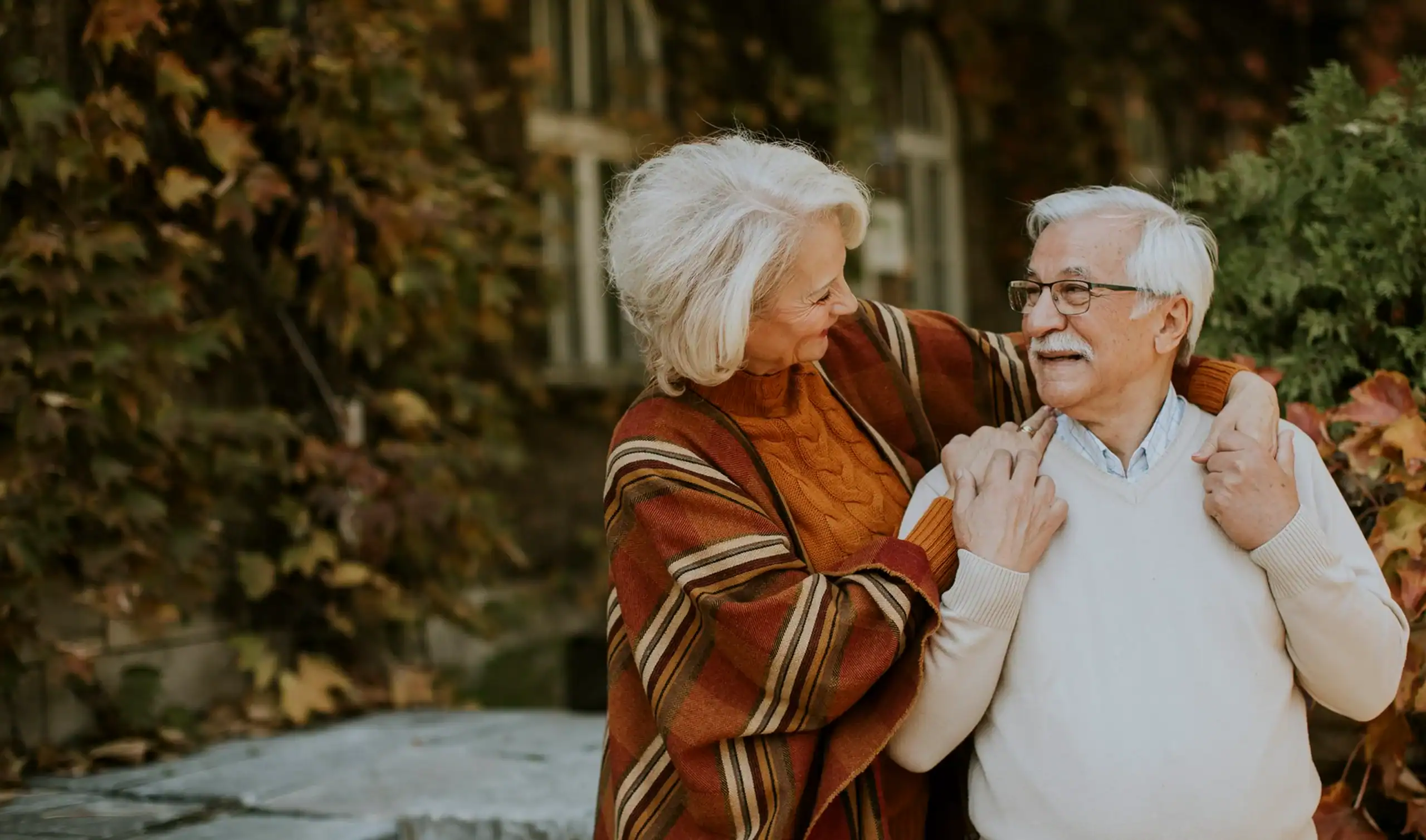 Elderly couple smiling warmly at each other outdoors