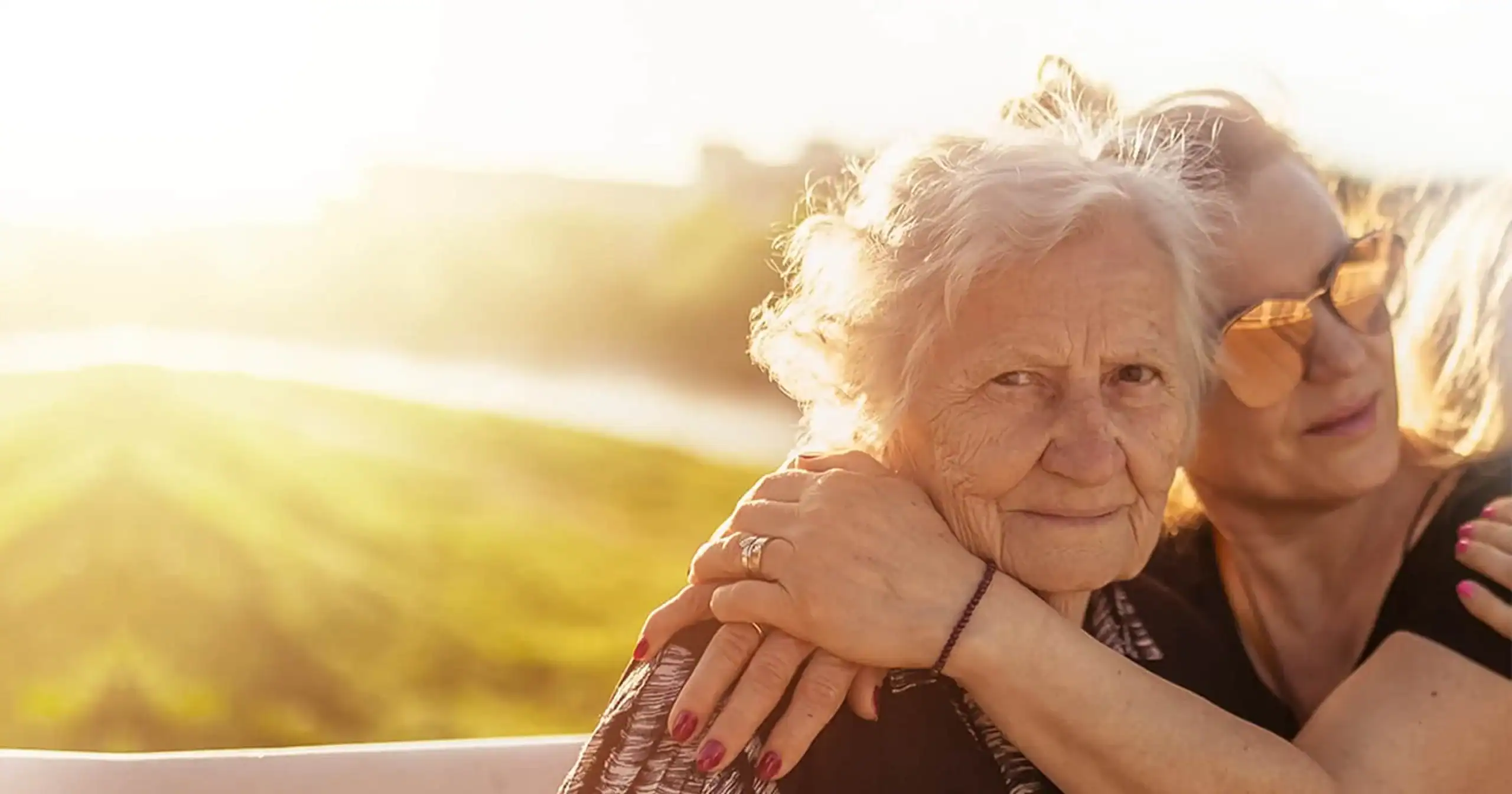 Two women embrace warmly in a sunlit outdoor